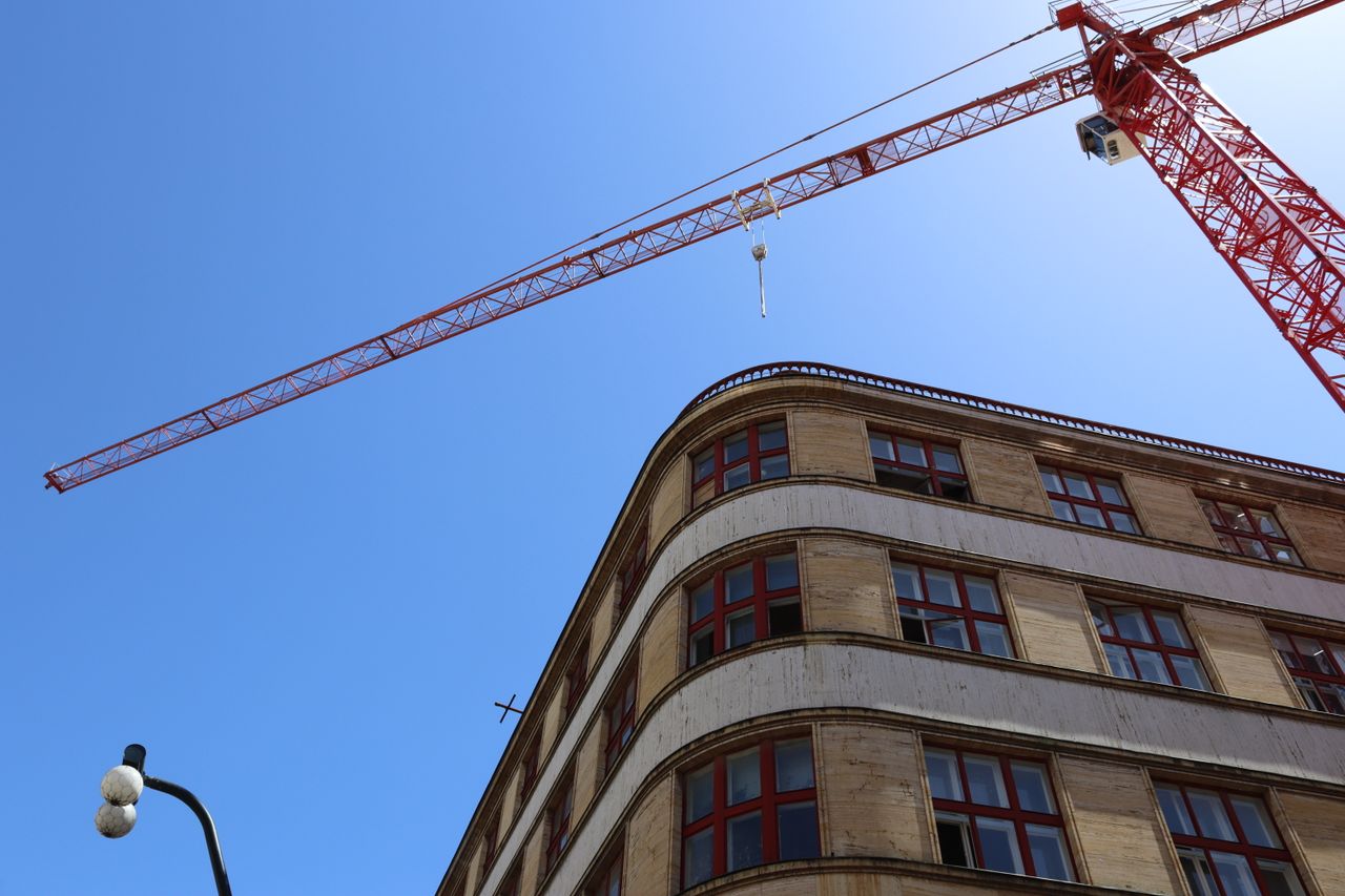 Low-angle view of a crane and building facade against a blue sky, perfect for construction themes.